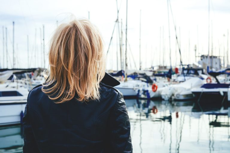 Portrait of an adult lady standing in a marina on yachts background. Back view.